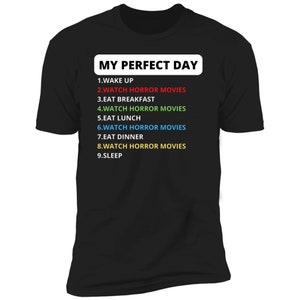 May include: Black t-shirt with white text that reads "MY PERFECT DAY" and a list of activities, including "WATCH HORROR MOVIES" in different colours.