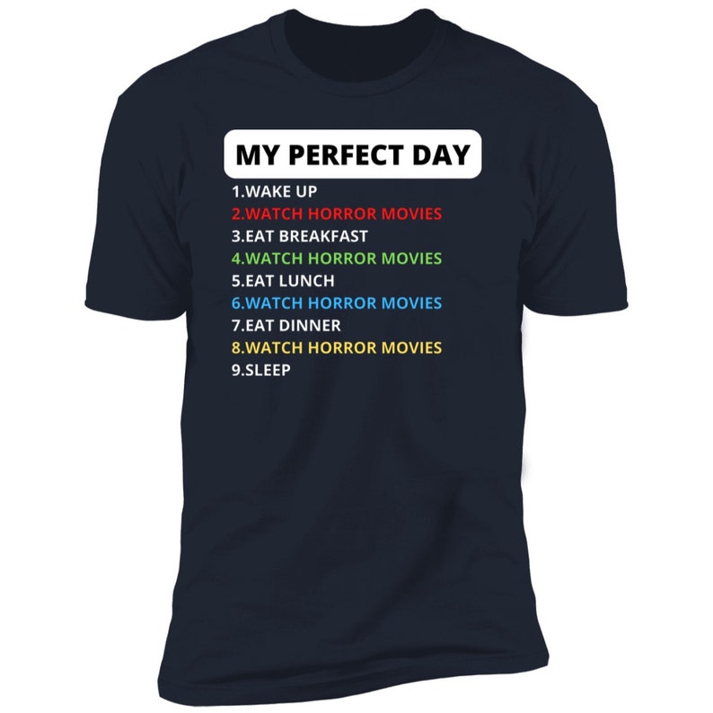 May include: A dark blue t-shirt with white text that reads "MY PERFECT DAY" and a list of activities, including "WATCH HORROR MOVIES" in different colours.