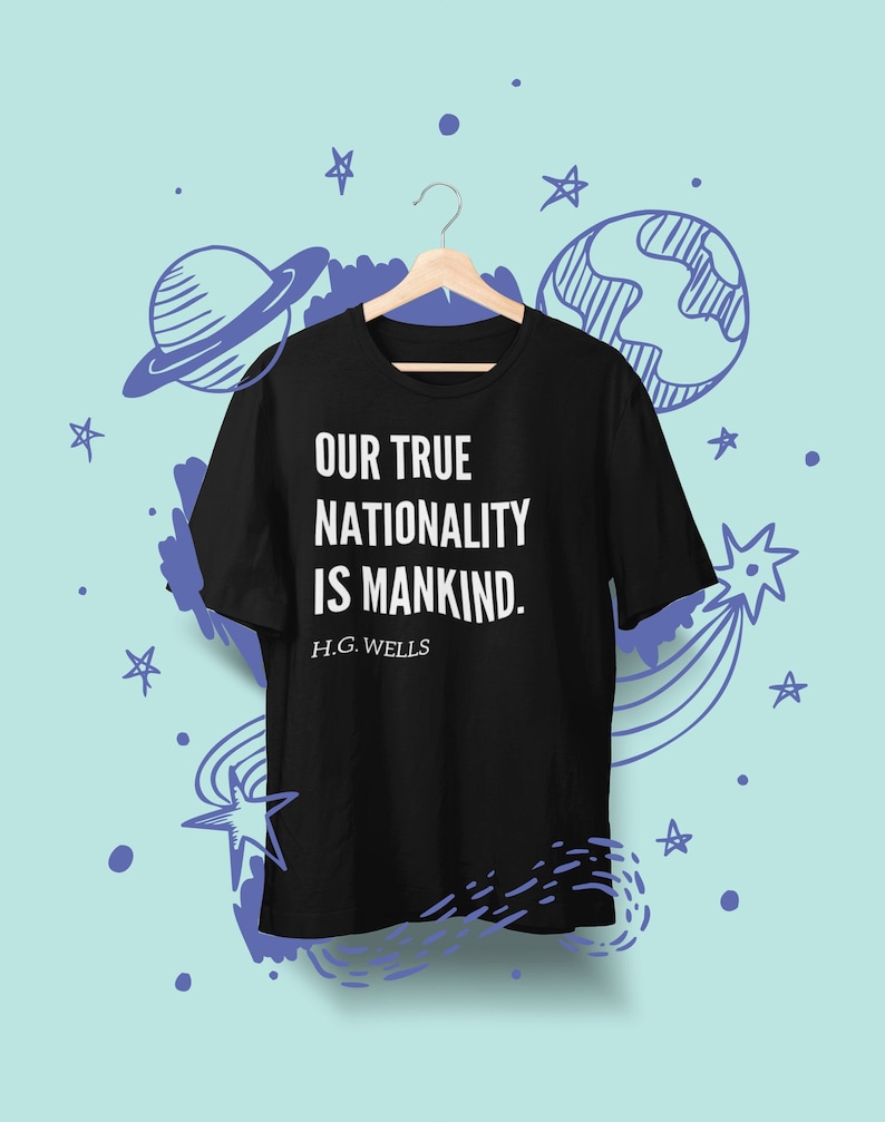 May include: Black t-shirt featuring the quote "Our true nationality is mankind." by H.G. Wells printed in white on the front. The shirt is hanging on a wooden hanger against a light blue background with a hand-drawn design of stars and planets.