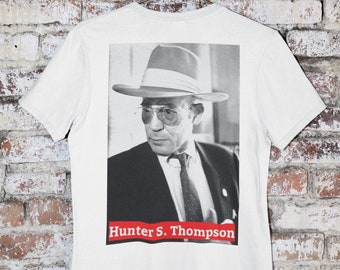May include: White t-shirt with a black and white photo of Hunter S. Thompson wearing a hat and sunglasses. The text "Hunter S. Thompson" is printed in red below the photo.
