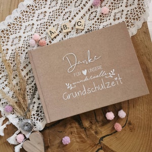 Könnte beinhalten: Ein braunes Fotoalbum mit dem Text "Danke für unsere wundervolle Grundschulzeit" in weißer Schrift. Das Album ist mit einem kleinen Herzen und einem floralen Design verziert.