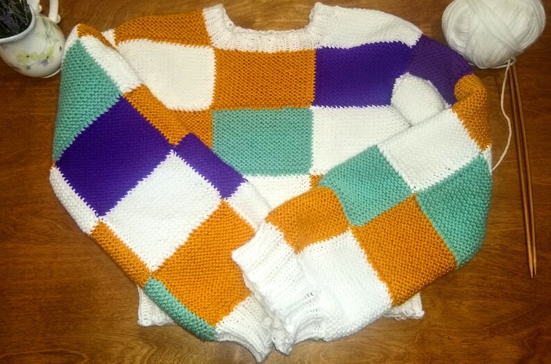 May include: A colourful knitted jumper with a checkered pattern in white, orange, purple, and green.