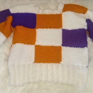 May include: A white, orange, purple and green checked knitted jumper.