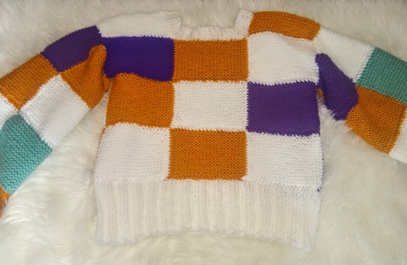 May include: A white, orange, purple and green checked knitted jumper.