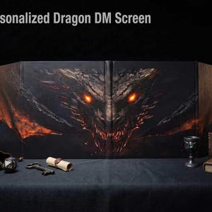 Puede incluir: Una pantalla de director de juego negra plegable con una cabeza de dragón detallada, ojos naranjas brillantes y acentos de fuego. El texto Personalized Dragon DM Screen es visible en la parte superior. Accesorios: dos dados, una llave, un pergamino, una copa y dos libros.