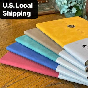 Peut inclure: Une pile de carnets colorés dans les tons rose, bleu, turquoise, beige, jaune et blanc. Le carnet supérieur est jaune avec un motif géométrique noir. Le texte "U.S. Local Shipping" est dans un encadré noir en haut à gauche.