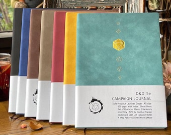 May include: A collection of colorful D&D 5e Campaign Journals. The journals have soft nubuck leather covers and A5 size. The journals are in various colors, including black, blue, brown, red, yellow, and teal. Each journal has a white band at the bottom with a dragon logo and text.
