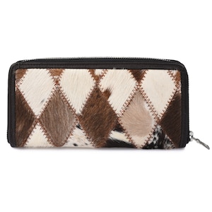 Puede incluir: Una cartera de cuero marrón con un diseño de patchwork de diferentes pieles de vaca de colores. La cartera tiene un cierre de cremallera y un tirador de cremallera marrón.
