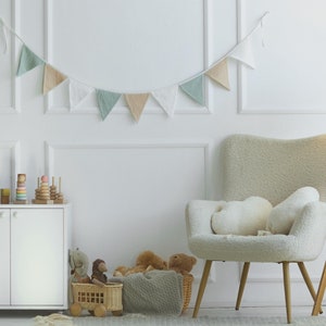 Puede incluir: Un armario blanco con dos puertas, un sillón blanco con un cojín blanco mullido, un suelo de madera y una lámpara de pie de madera con una pantalla blanca. Hay animales de peluche y juguetes de madera en el suelo delante del armario.