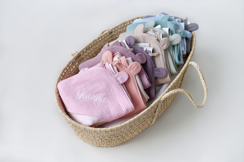 May include: A wicker basket filled with a variety of soft, pastel-colored baby blankets. The blankets have embroidered ears and the top blanket is personalized with the name "Gianna".