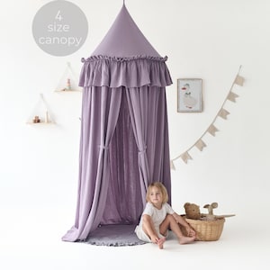 May include: A lavender canopy with a ruffled edge and draped curtains. The canopy is cone-shaped and has the text "4 size canopy" in a circle above it. A young child sits near a woven basket with stuffed animals.