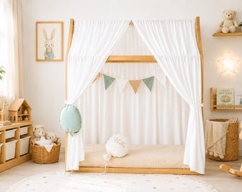 May include: A wooden house-shaped floor bed frame with white fabric curtains, a beige mattress, and a decorative bunting banner. The bed features a round sage green pillow and a white balloon-shaped pillow with the word Hello embroidered on it.