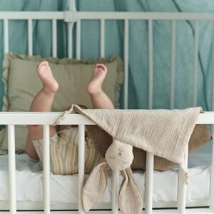 A baby's feet are visible in a crib, with a stuffed bunny toy resting on the bed.