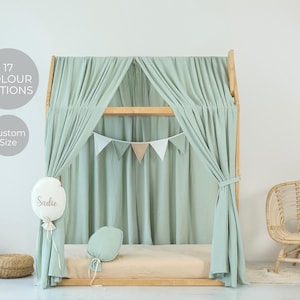 Puede incluir: Una cama con dosel de color verde claro con una pancarta triangular blanca y beige colgada sobre la cama. La cama tiene un colchón marrón claro y una almohada verde claro. La cama está en una habitación con una pared blanca y una silla de mimbre con una almohada blanca.