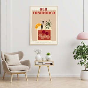May include: A minimalist poster with the text "Old Fashioned" in red and white letters. The poster features a stylized illustration of an Old Fashioned cocktail with a cherry, orange slice, and two straws. The background is a light brown color.