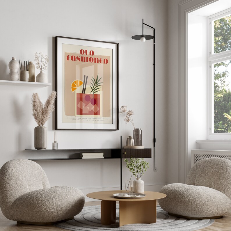 May include: A minimalist living room interior with two beige armchairs, a round coffee table, and a black wall-mounted lamp. A framed poster with the text "Old Fashioned" and a stylized illustration of a cocktail is hanging on the wall.