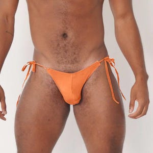 May include: Orange bikini bottom with tie sides. The swimwear is a solid color and appears to be made of a smooth fabric. The background is a plain white.