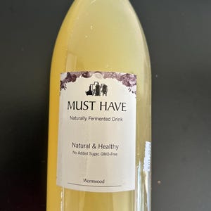 May include: A clear bottle containing a yellow liquid. The label says "MUST HAVE Naturally Fermented Drink Natural & Healthy No Added Sugar, GMO-Free Wormwood". The bottle has a white cap.
