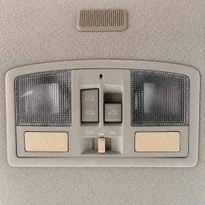 Peut inclure: Une console de plafond de voiture beige avec deux lentilles d'éclairage texturées rectangulaires, deux boutons carrés et un panneau de commande central avec trois icônes de toit ouvrant. Un petit interrupteur coulissant indique OFF et ON.