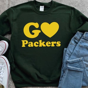 May include: Green sweatshirt with a yellow "G" and heart, and the text "Packers" in yellow.