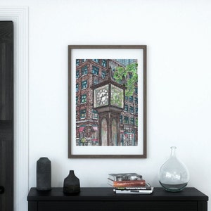 May include: Framed art print featuring a detailed watercolor illustration of a vintage street clock. The clock is brown with a glass face, set against a backdrop of brick buildings and greenery. The artwork is displayed on a white wall.