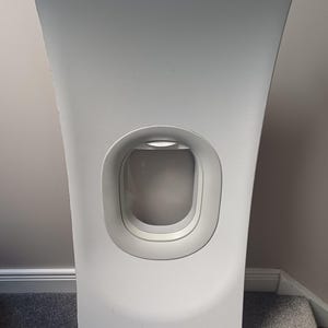 May include: A white, curved panel with a rectangular window-like opening. The panel has a textured surface and a rounded top. The window has a rounded frame. The panel is likely a decorative or architectural element.