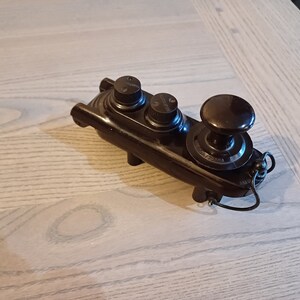 May include: A vintage, dark brown control panel with three knobs and a larger dial. The panel has a rectangular base with rounded edges and a small wire extending from the side. The knobs have small markings.