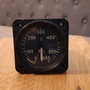 May include: A black circular gauge with a white needle and a black face. The gauge has white markings for 0, 100, 200, 300, 400, 500, and 600. The needle is pointing to 400.