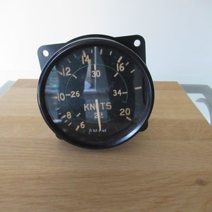 May include: A black vintage aircraft airspeed indicator with a circular gauge. The gauge has white and green markings for speed in knots, ranging from 6 to 34. The text "KNOTS" is visible, along with other markings.