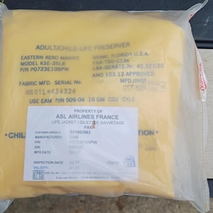 May include: A yellow adult and child life preserver sealed in a clear plastic bag. The packaging features printed text including ADULT/CHILD LIFE PRESERVER, EASTERN AERO MARINE, MODEL KSE-35LB, and PROPERTY OF ASL AIRLINES FRANCE LIFE JACKET.