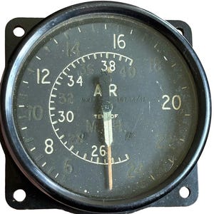 Op de afbeelding: Een vintage zwarte ronde luchtvaartmeter met een vierkante montageflens. De wijzerplaat heeft witte numerieke markeringen van 6 tot 24 en een binnenschaal van 26 tot 40. Tekst bevat AR, MK 1, 16784/42 en TEMP OF M.H. Een enkele naald wijst naar boven.