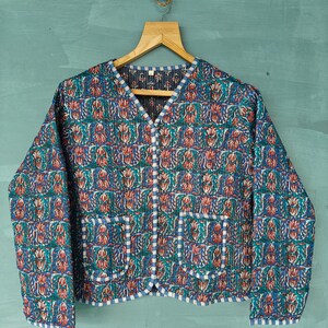 May include: A blue quilted jacket with a floral print and white trim. The jacket has a V-neck and button closure. It features two patch pockets on the front.
