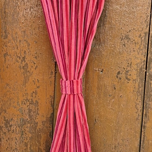 May include: A pair of pink and red striped curtains hanging from a metal rod. The curtains are made of a soft, velvety fabric.