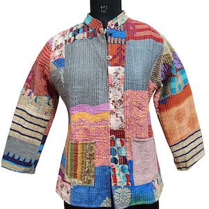 Könnte beinhalten: Eine Patchwork-Jacke mit Stehkragen und Knopfverschluss. Die Jacke hat eine Vielzahl von bunten Stoffflicken in Blau-, Rosa-, Orange- und Grautönen. Sie hat zwei Vordertaschen und dreiviertellange Ärmel.