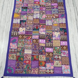 Könnte beinhalten: Eine violette Patchwork-Decke mit einer Vielzahl von bunten Stickmustern und Verzierungen. Die Decke hat einen Fransenrand und ist aus einem weichen, komfortablen Stoff gefertigt.