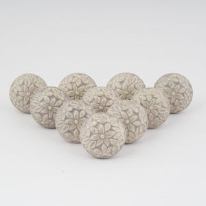 Könnte beinhalten: Zehn graue Keramikknöpfe mit einem erhabenen Blumenmuster. Die Knöpfe sind in einem Halbkreis angeordnet.