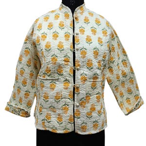 May include: A white quilted jacket with a floral print in yellow and green. The jacket has a mandarin collar, a button closure, and two pockets.