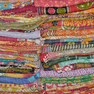 Könnte beinhalten: Ein Stapel bunter Kantha-Steppdecken aus recycelten Saris. Die Decken sind in verschiedenen Mustern und Farben übereinander gelegt, darunter Rot, Grün, Blau, Gelb und Orange.