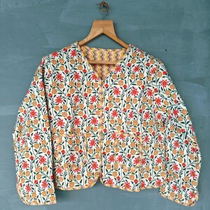 May include: A white quilted jacket with a floral print in shades of red, yellow, and green. The jacket has a button closure and two pockets.