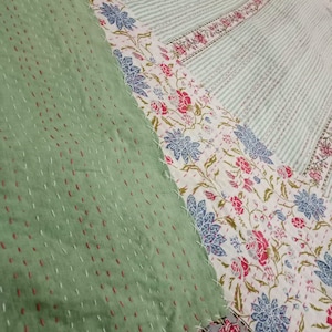 Könnte beinhalten: Eine Patchwork-Decke mit einem floralen Muster in Grün, Weiß und Blau. Die Decke besteht aus verschiedenen Stoffen, die zusammengenäht wurden und so ein einzigartiges und strukturiertes Aussehen erzeugen.