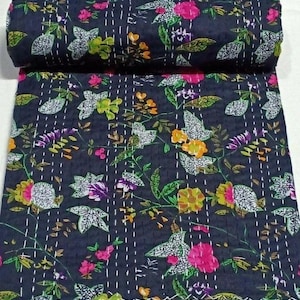 May include: A dark blue floral quilt with a rolled-up section at the top. The quilt features a repeating pattern of flowers and leaves in shades of pink, yellow, green, and white. White stitching is visible throughout the quilt.