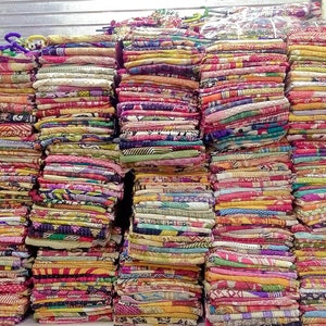 Könnte beinhalten: Ein Stapel bunter Kantha-Steppdecken, hergestellt aus recycelten Saris, mit komplizierten Mustern und Designs. Die Decken sind ordentlich gefaltet und gestapelt und bilden ein lebendiges und strukturiertes Display.