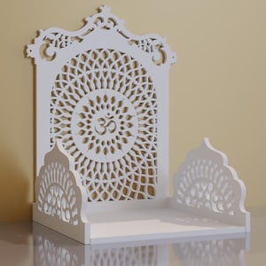 May include: White wooden altar with intricate cut-out designs. The altar features a central circular pattern with the Om symbol, and a shelf. The design is symmetrical and ornate, suitable for spiritual practices.