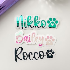 May include: Three personalized pet name stickers with paw prints. The names are Nikko, Bailey, and Rocco. The stickers are on a white background.