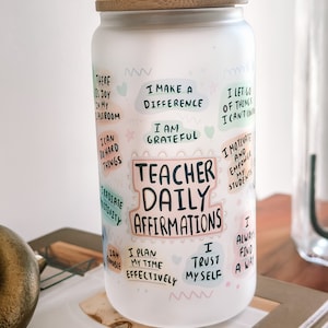 May include: White ceramic tumbler with a bamboo lid and a straw. The tumbler has a colorful design with the text "Teacher Daily Affirmations" and positive affirmations for teachers.