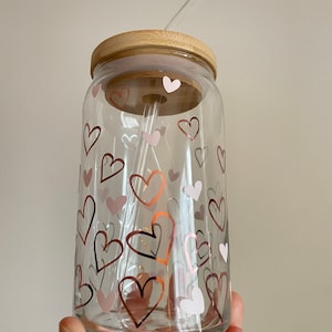 May include: A clear glass jar with a wooden lid and a straw. The jar is decorated with pink and gold hearts.