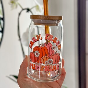 May include: A glass jar with a bamboo lid and a straw. The jar has a graphic of pumpkins with the text "Farm Fresh Pumpkins" in pink and orange letters.