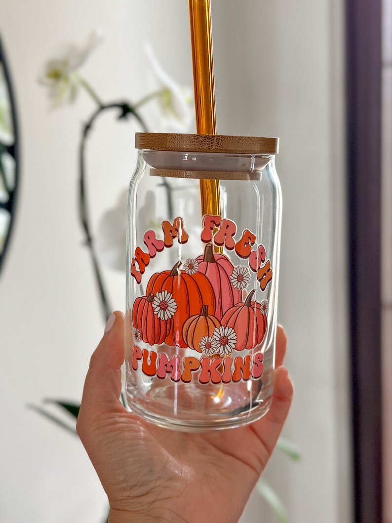 May include: A glass jar with a bamboo lid and a straw. The jar has a graphic of pumpkins with the text "Farm Fresh Pumpkins" in pink and orange letters.