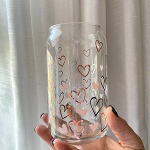 May include: A clear glass can with a pattern of pink, white, and brown hearts. The can is perfect for holding beverages.