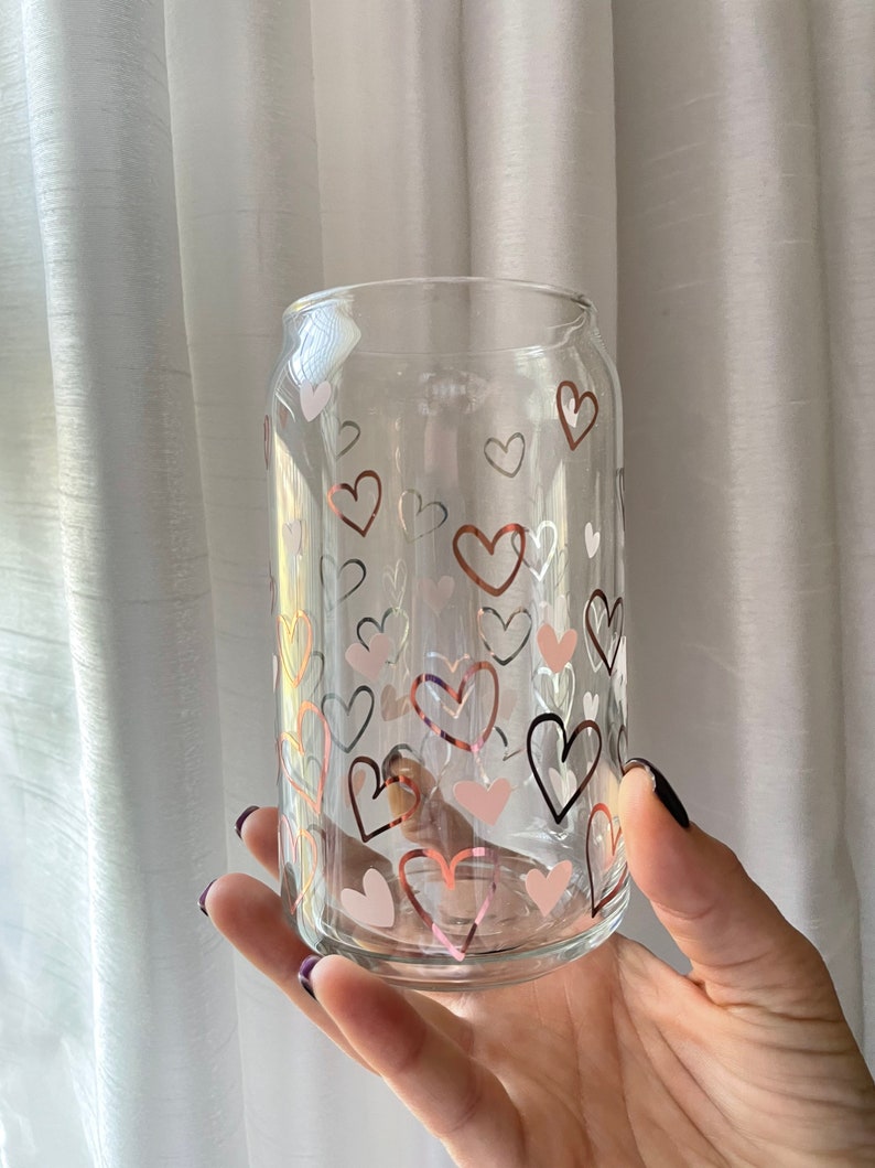 May include: A clear glass can with a pattern of pink, white, and brown hearts. The can is perfect for holding beverages.